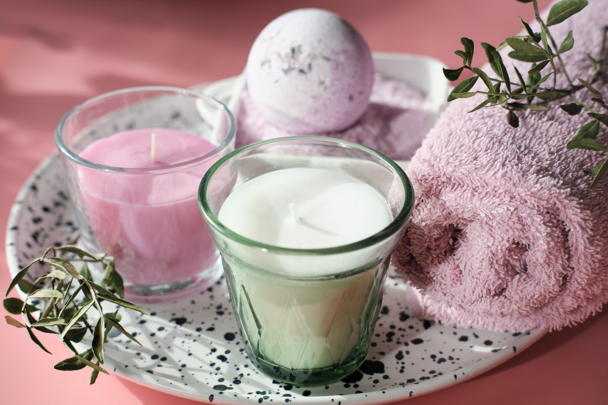 scented soy wax candles and bath bomb and pink towel on pink background. wellness set