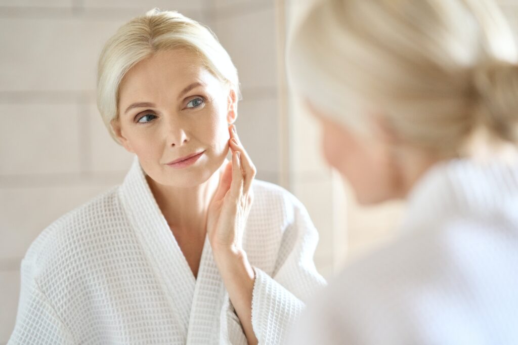 Beautiful mid age blond woman standing looking at mirror. Skincare. How Diet Affects Skin Health