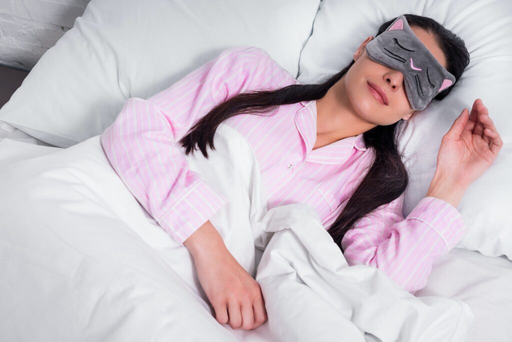 portrait of woman in pink pajamas and sleeping mask sleeping in bed at home How Fitness Enhances Natural Beauty