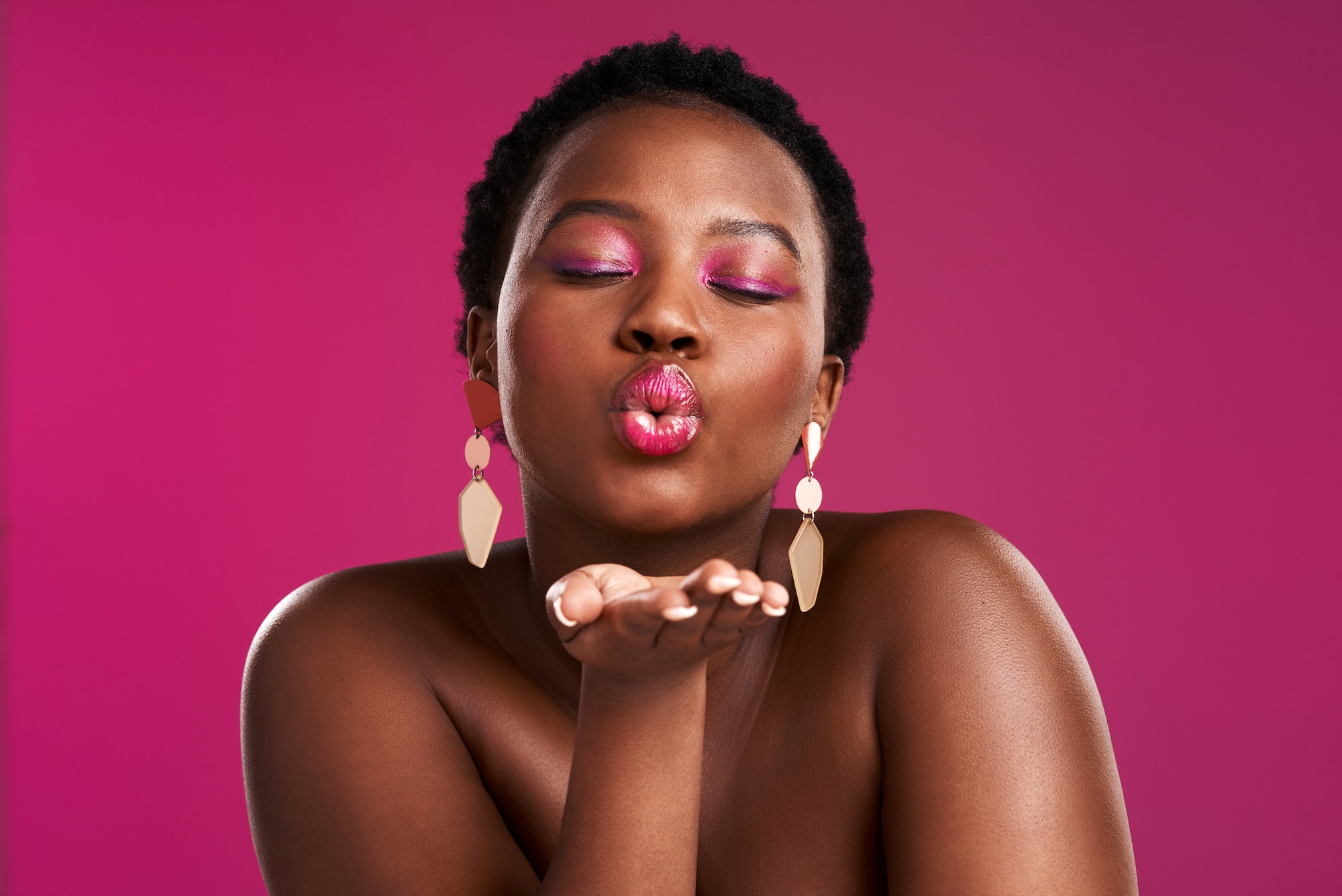 Studio shot of a beautiful young woman blowing a kiss against a pink background