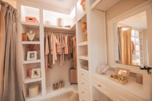 Gorgeous luxury wardrobe closet with pale pink pastel clothes on hangers and heeled shoes on shelf