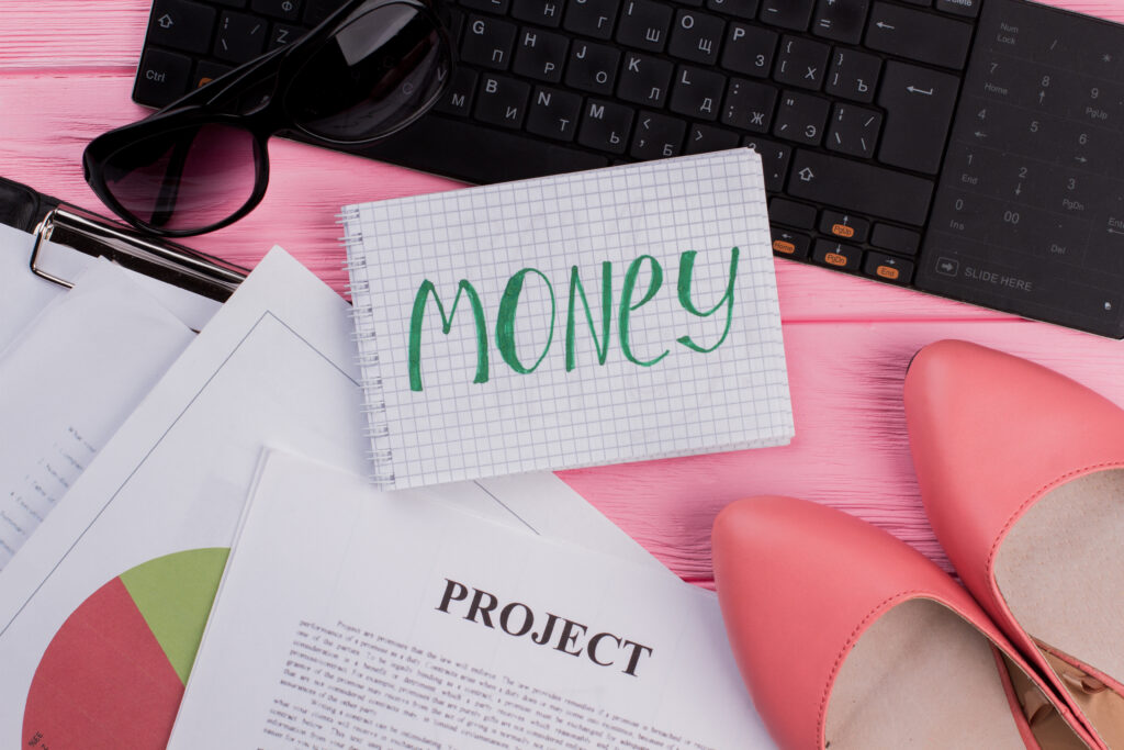 Money written on notepad and women accessories on pink background.