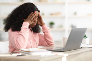 Stressed black woman sitting in front of laptop, touching head