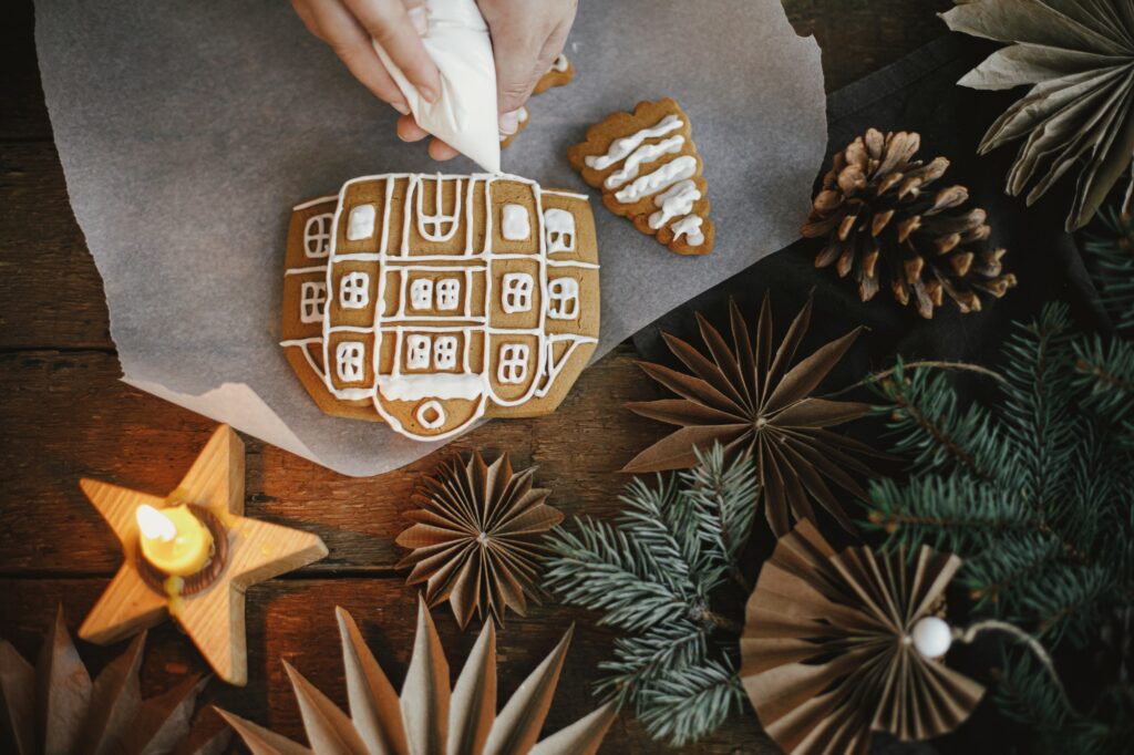 Decorating christmas cookies with icing on rustic table flat lay. Making gingerbread house