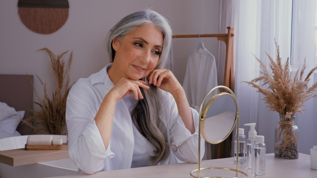 Caucasian 60s aged senior mature lady old gray-haired 50s woman female looking at mirror reflection
