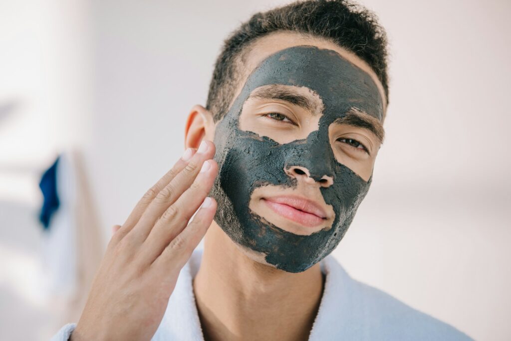 confident young man applying face mask with hand and looking at camera Essential Skincare Tips for Winter