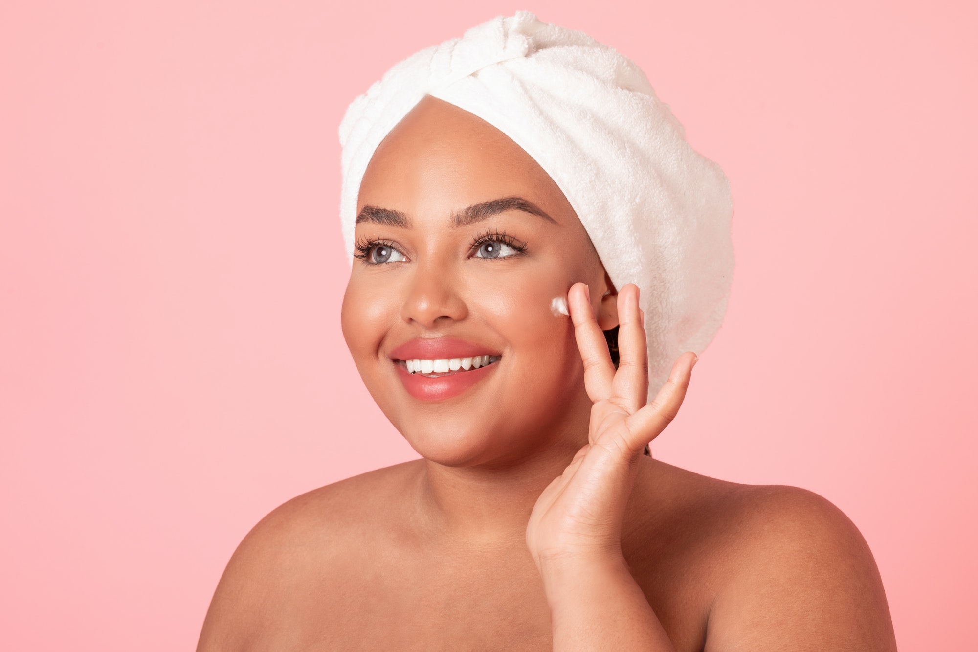 Skin care concept. Closeup portrait of black plus size lady applying moisturizing cream on face