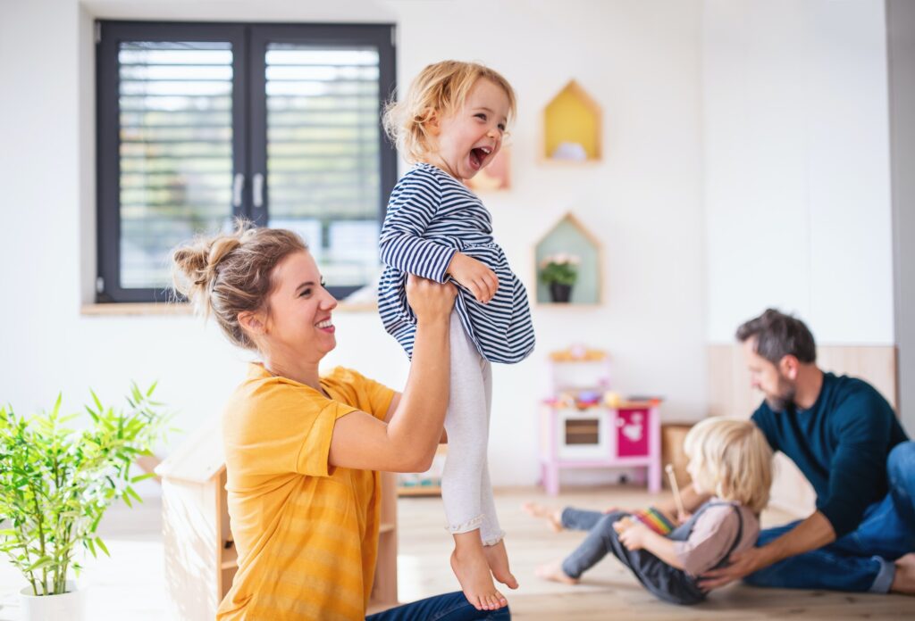 Young family with two small children indoors in bedroom having fun.