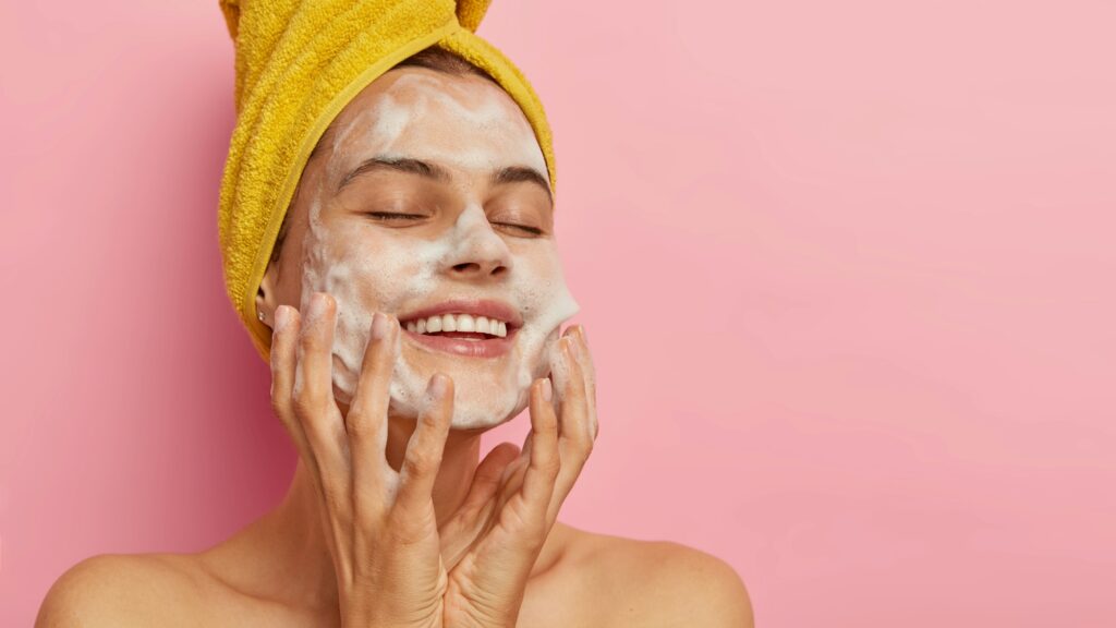 Feminity and hygiene concept. Young delighted female washes face with soap, smiles happily, closes How to Properly Wash Your Face to Prevent Breakouts