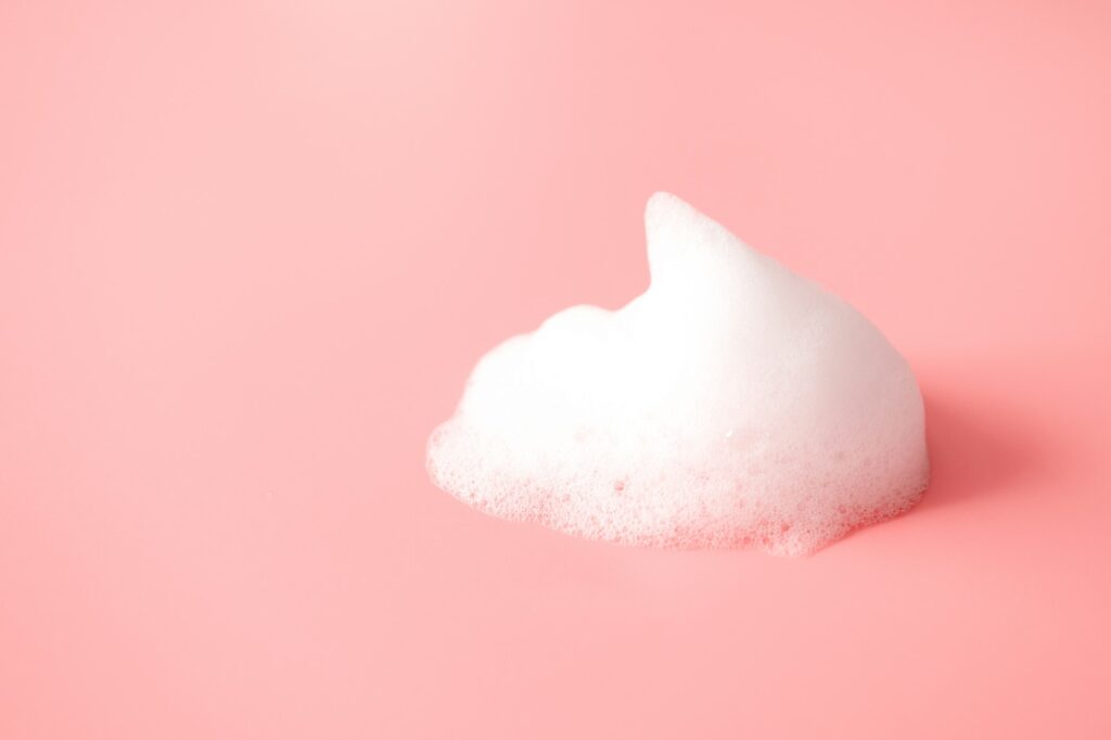 White foam smear from soap, shampoo or cleanser on pink background How to Properly Wash Your Face to Prevent Breakouts