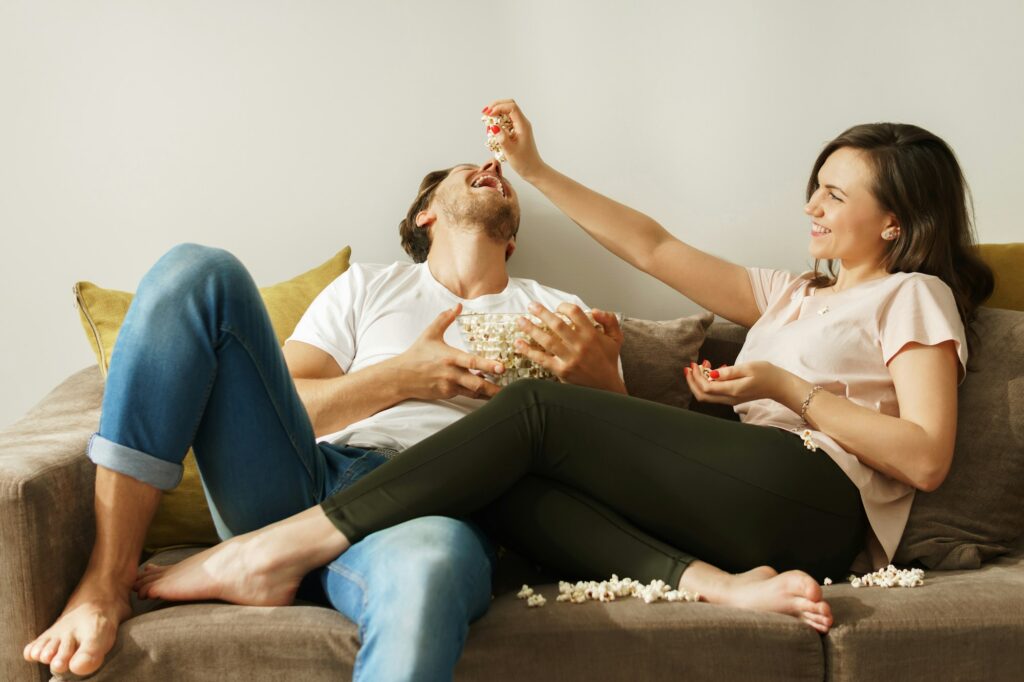 Happy couple eating popcorn and watching movie at home At-Home Date Night Ideas for Couples