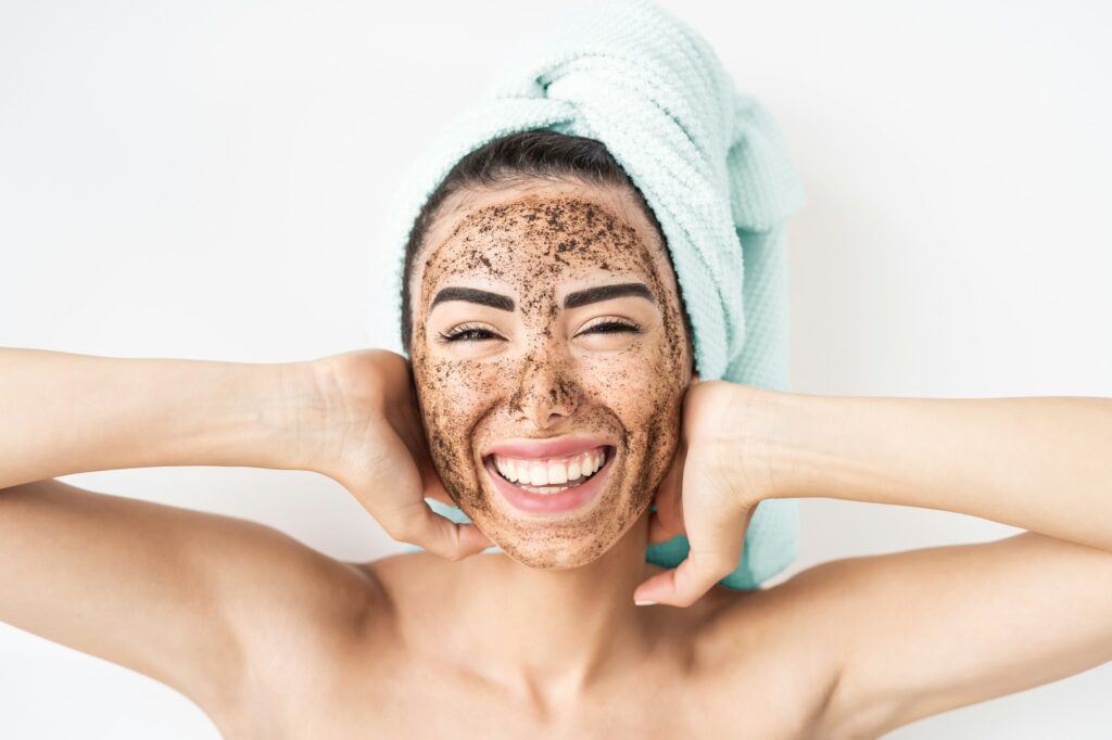 Young smiling woman applying coffee scrub mask on face DIY Facial at home