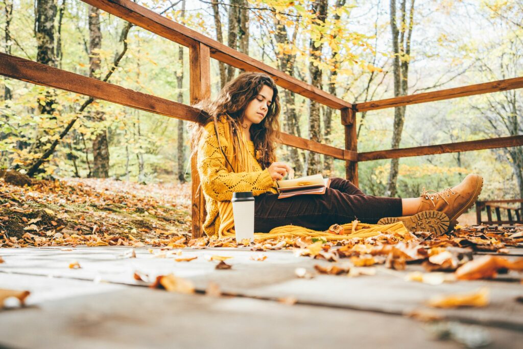 Brunette woman in yellow sweater sitting on a fallen autumn leaves in a park