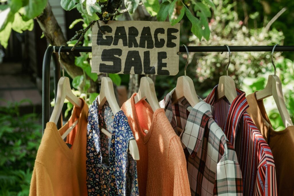 Garage sale, clothes for sale hanging on hanger outdoors.