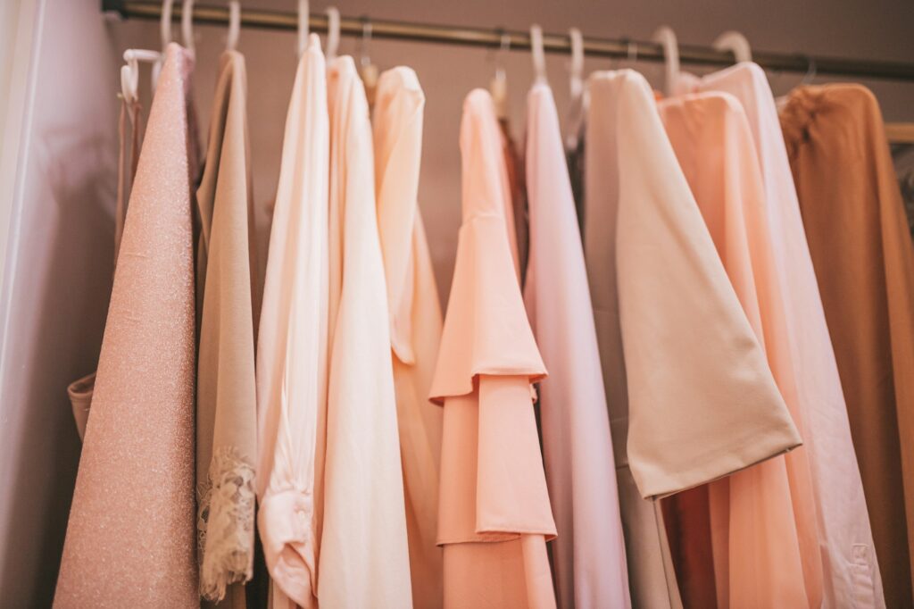 Gorgeous luxury wardrobe closet with pale pink pastel clothes on hangers and heeled shoes on shelf