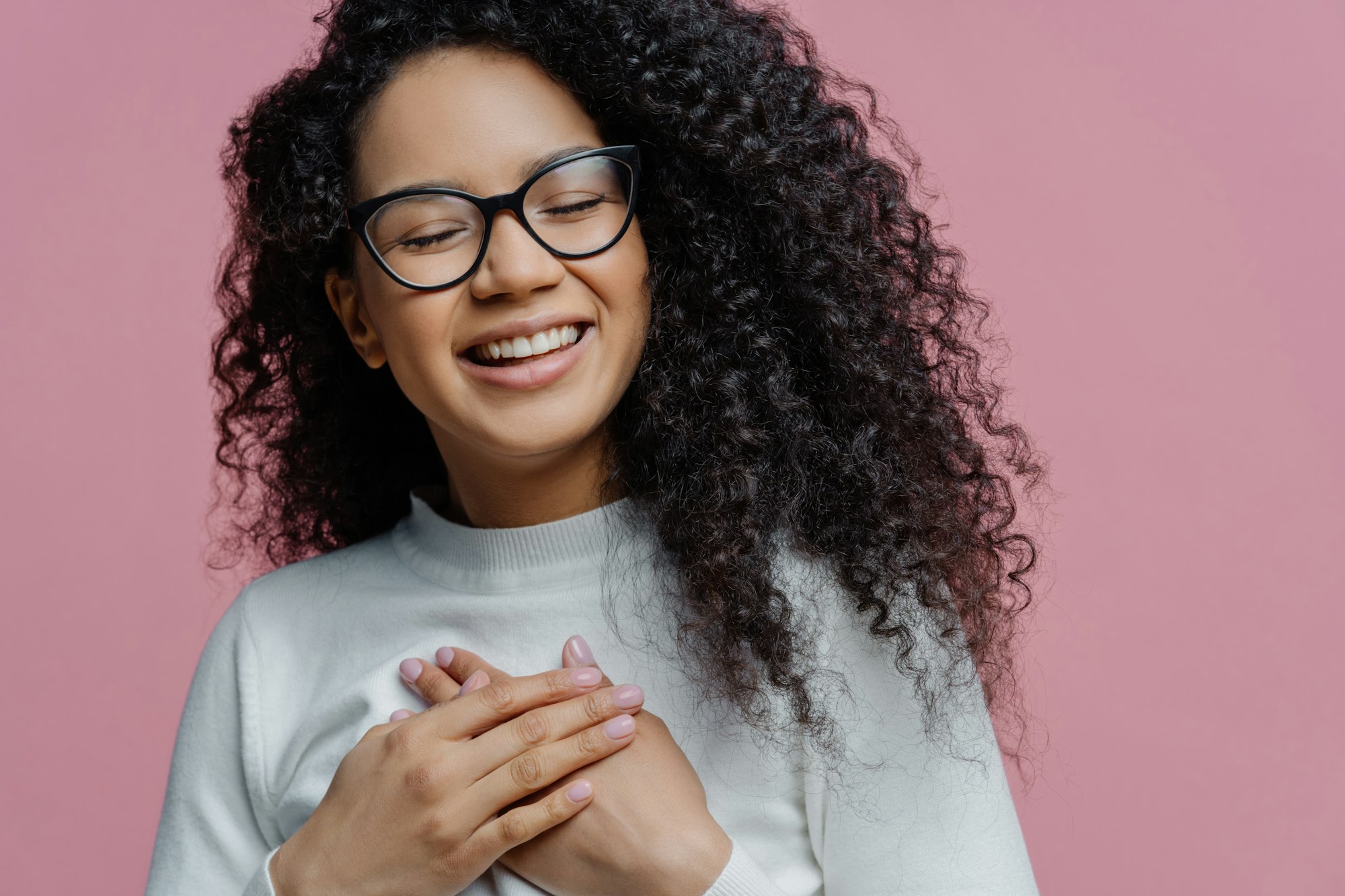 Happy Afro American woman, grateful and sincere, smiles, gestures thanks, wearing glasses